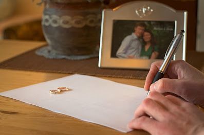 Hand writing a card on a wooden table beside a framed photo and vase