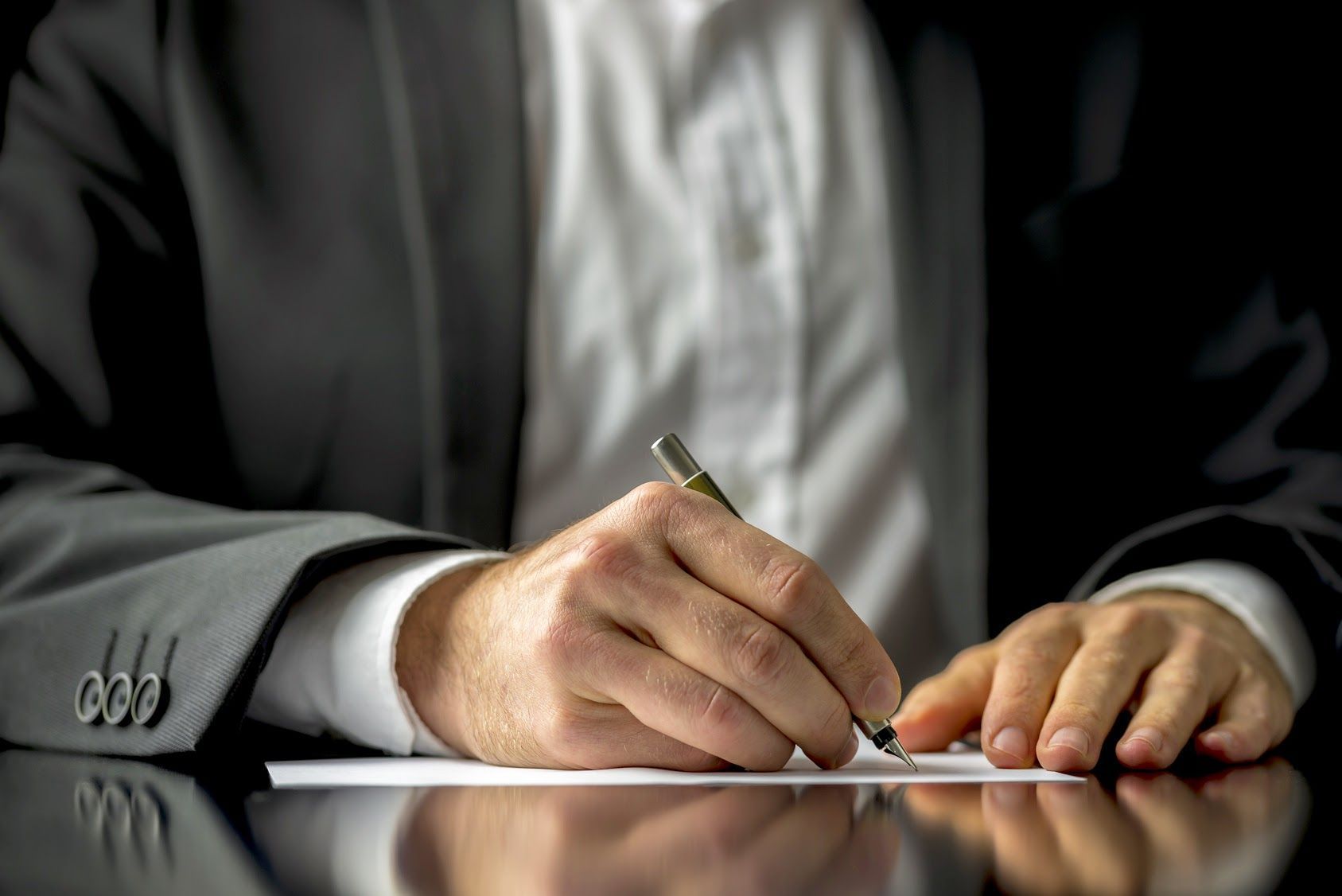 Hands in a gray suit signing a document with a pen on a desk