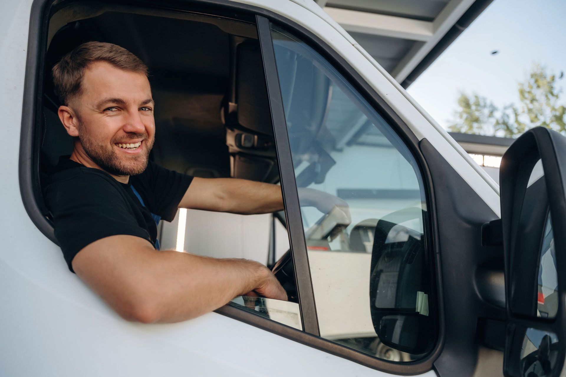 Smiling man leaning out of a white truck driver’s window with the door open