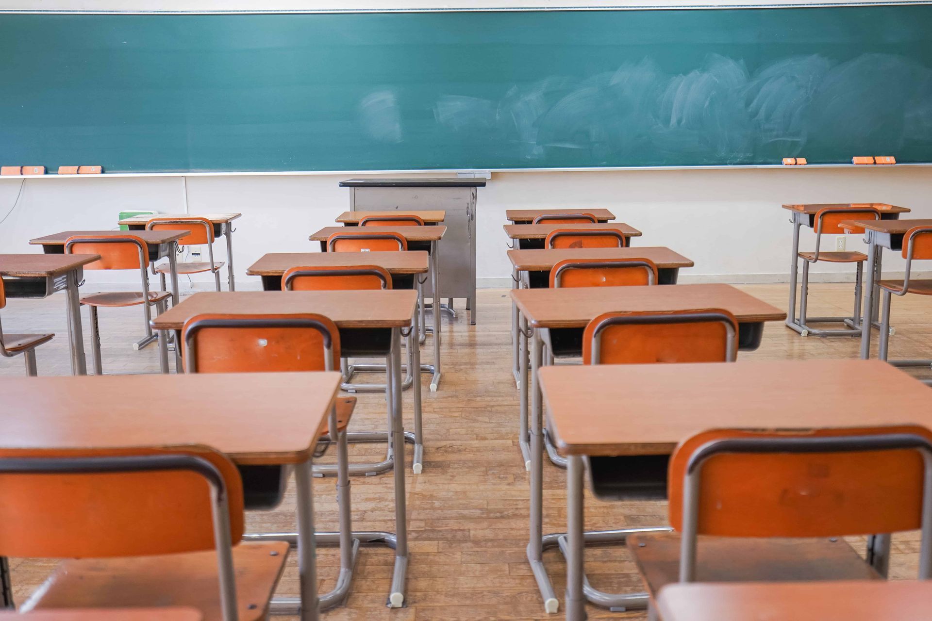 Empty classroom with rows of wooden desks facing a green chalkboard.