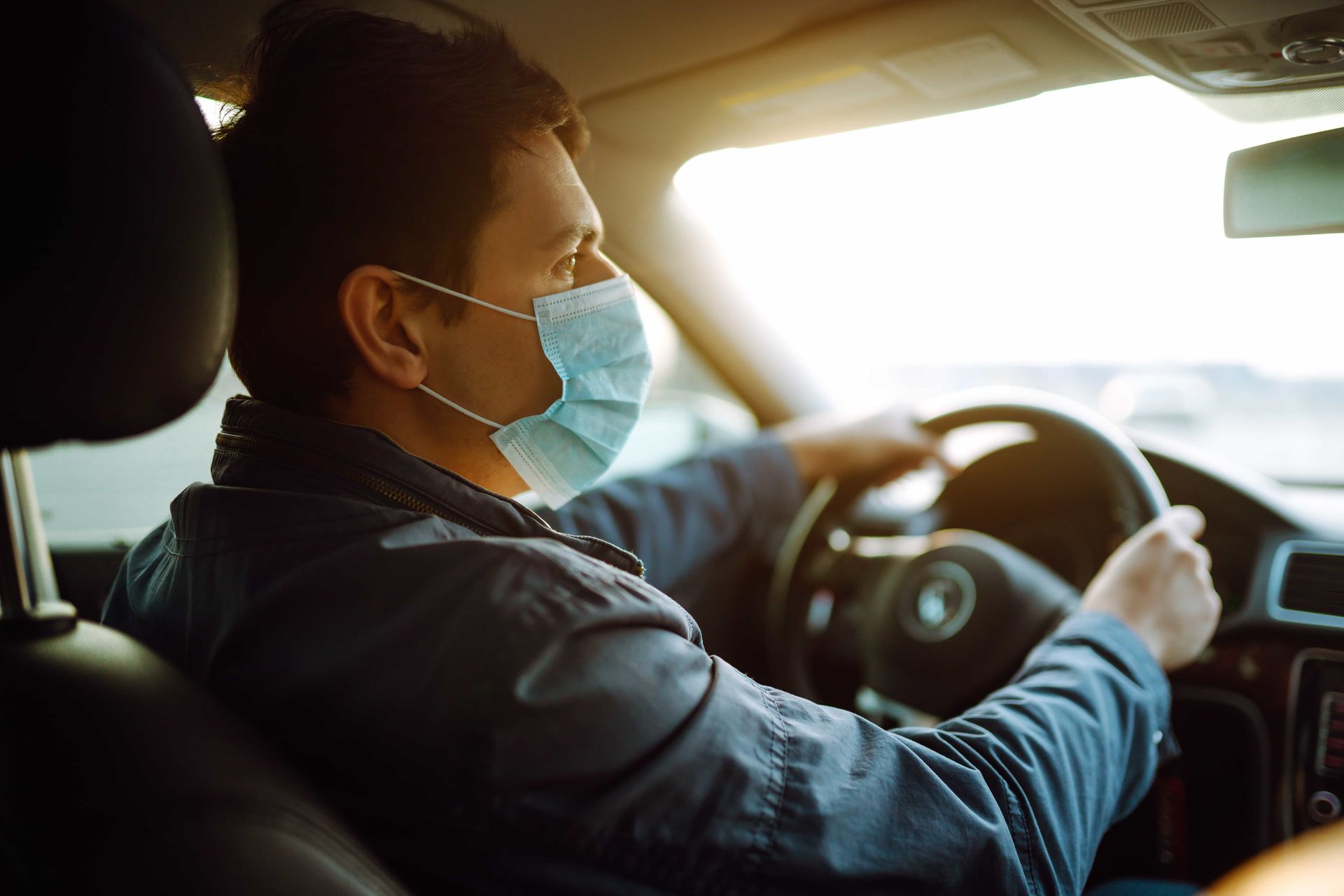 Masked driver steering a car in bright sunlight