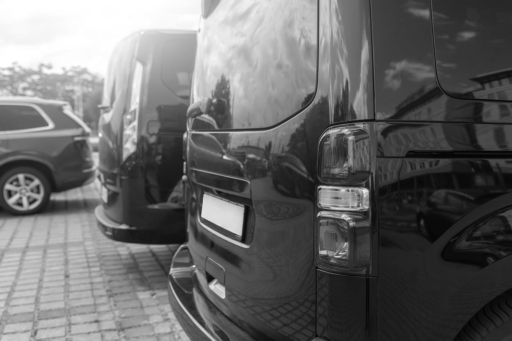 Black van parked in a lot at sunset with a red taillight and another vehicle ahead
