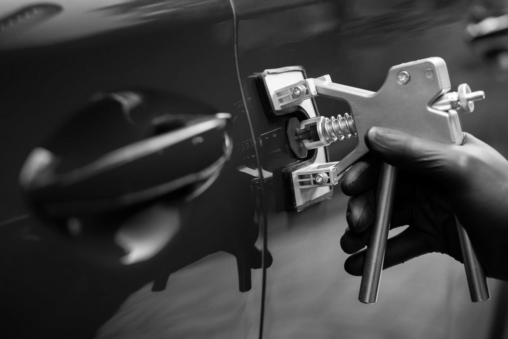 Gloved hand using a lock pick tool to unlock a red car door