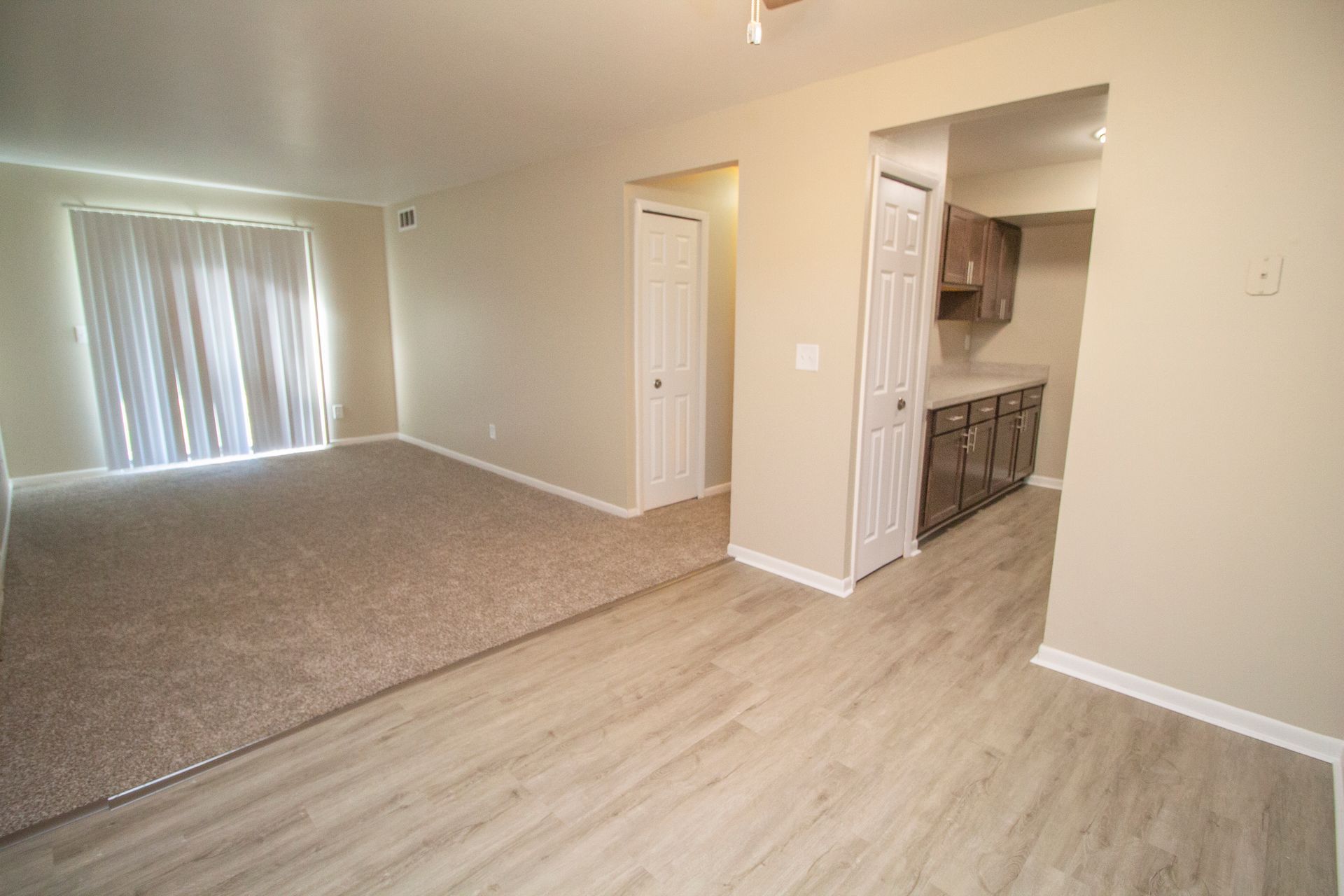 A living room with hardwood floors and a sliding glass door leading to a kitchen.