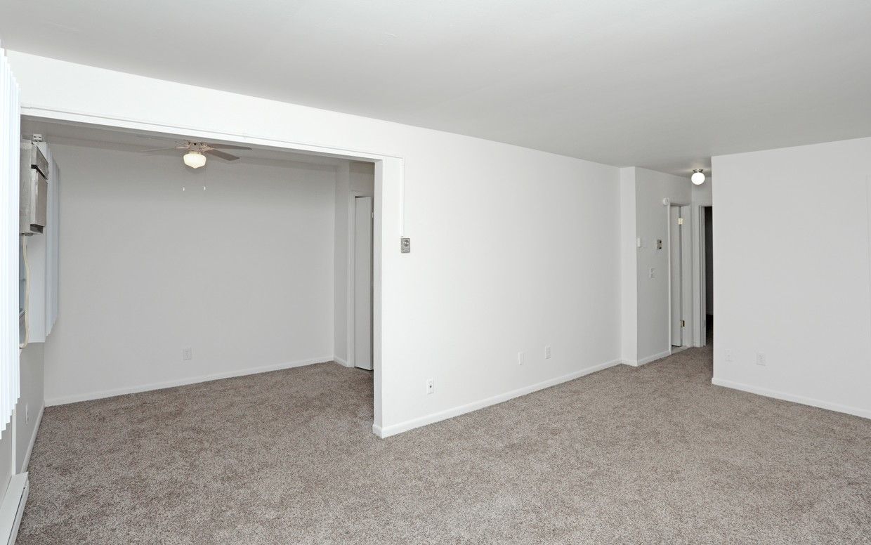 An empty living room with white walls and a ceiling fan.