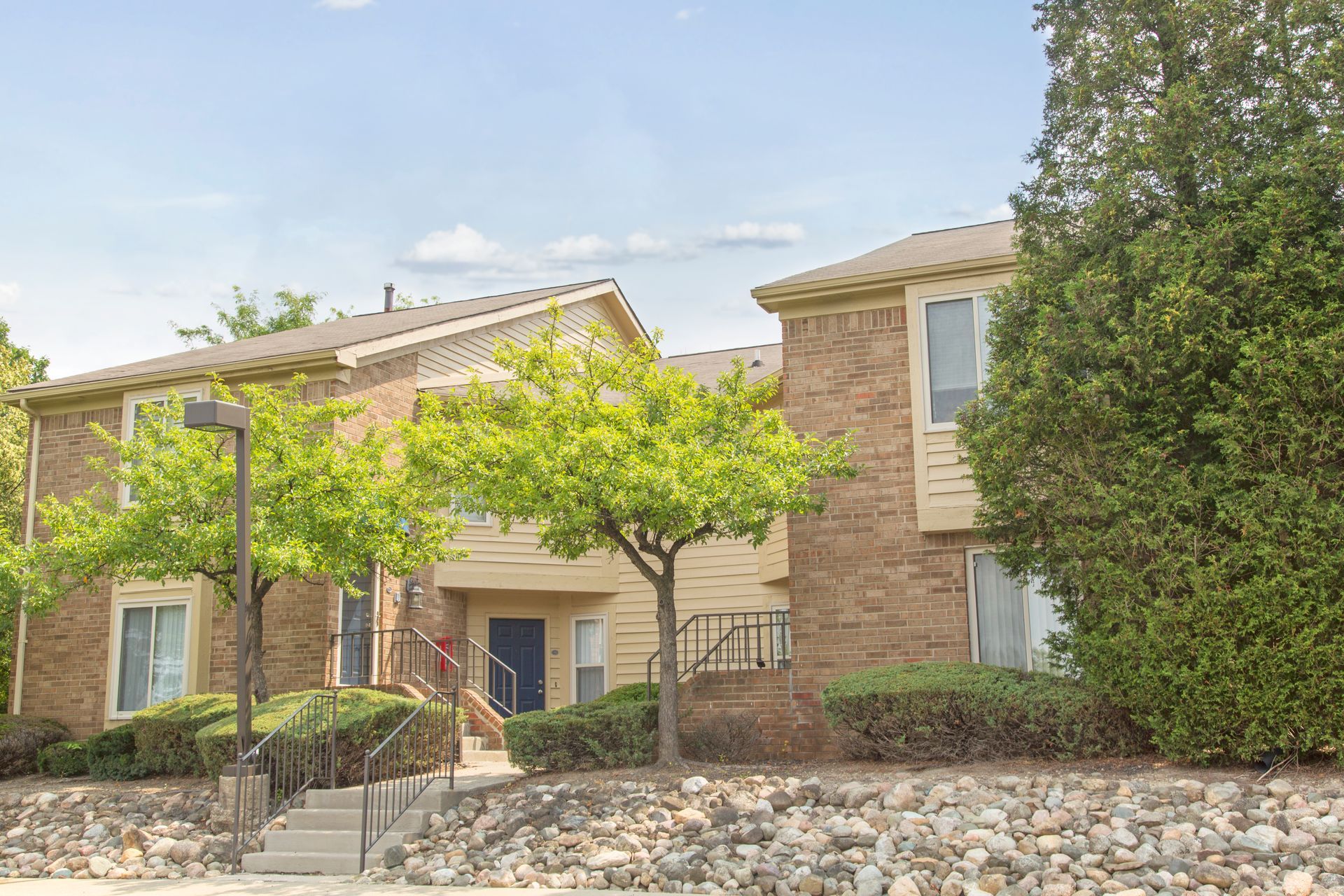 A brick apartment building with stairs leading up to it and trees in front of it.