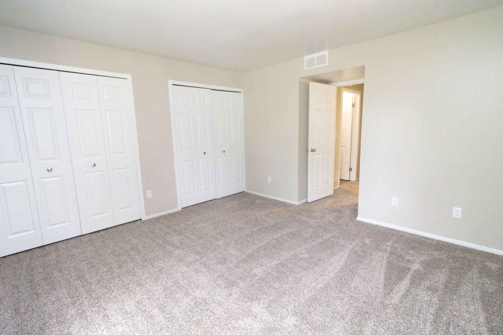 An empty bedroom with a lot of closets and a carpeted floor.