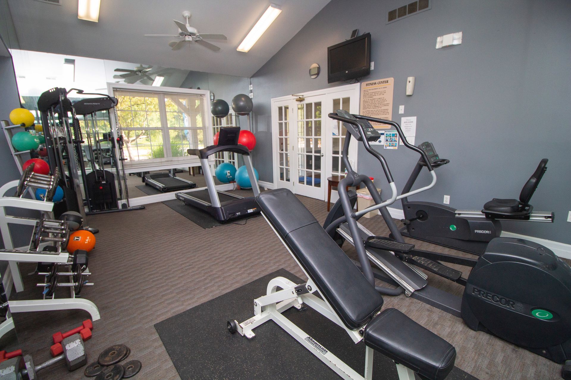 A gym with a bench , treadmill , elliptical and other equipment