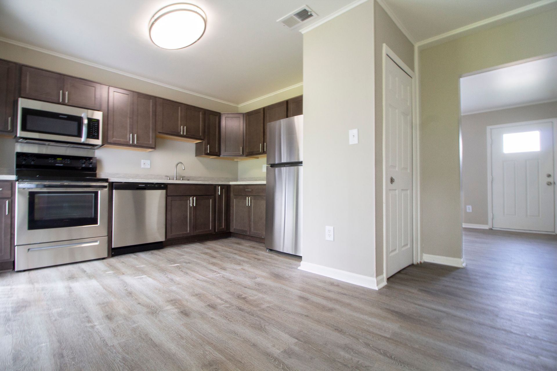 An empty kitchen with stainless steel appliances and wooden floors.