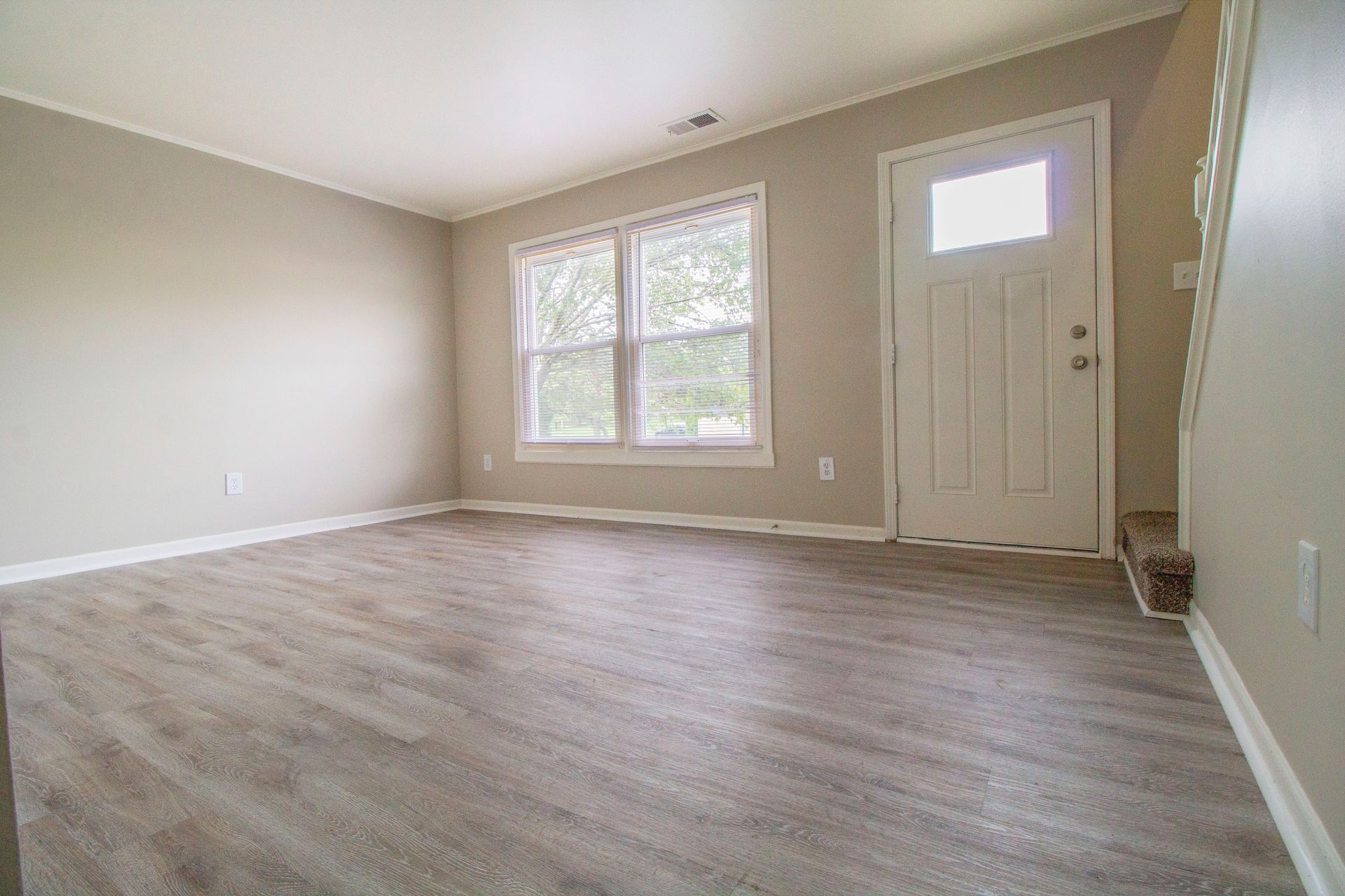 An empty living room with hardwood floors and a white door.