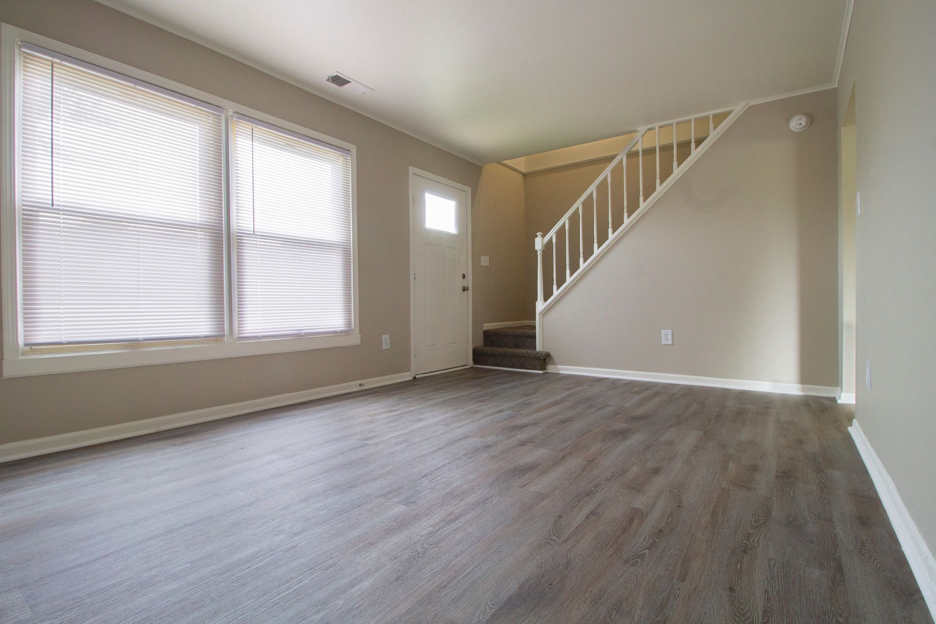 An empty living room with hardwood floors and stairs leading up to the second floor.