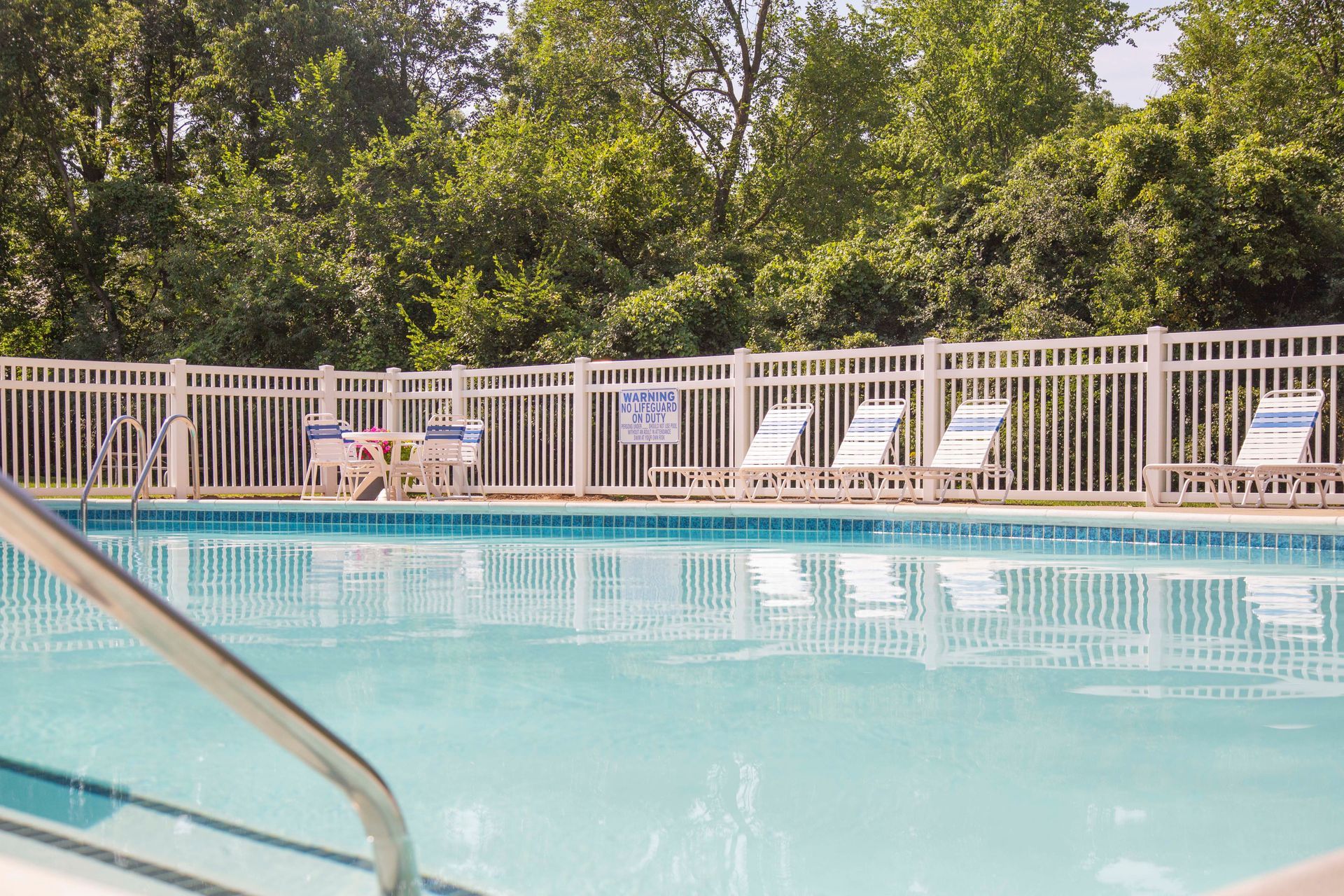 A large swimming pool surrounded by a white fence and chairs.
