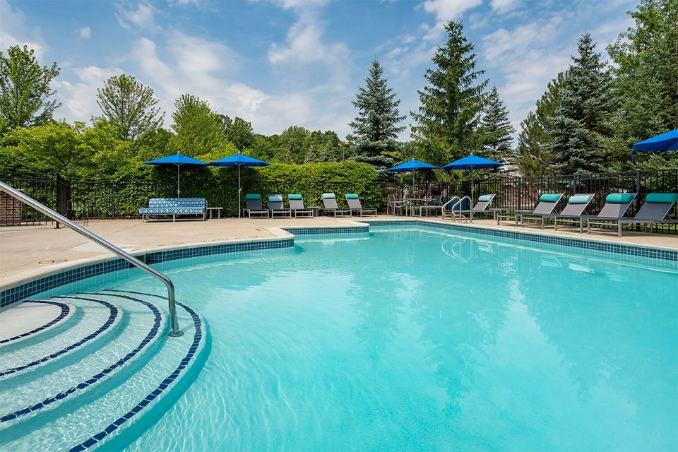 A large swimming pool surrounded by chairs and umbrellas on a sunny day.