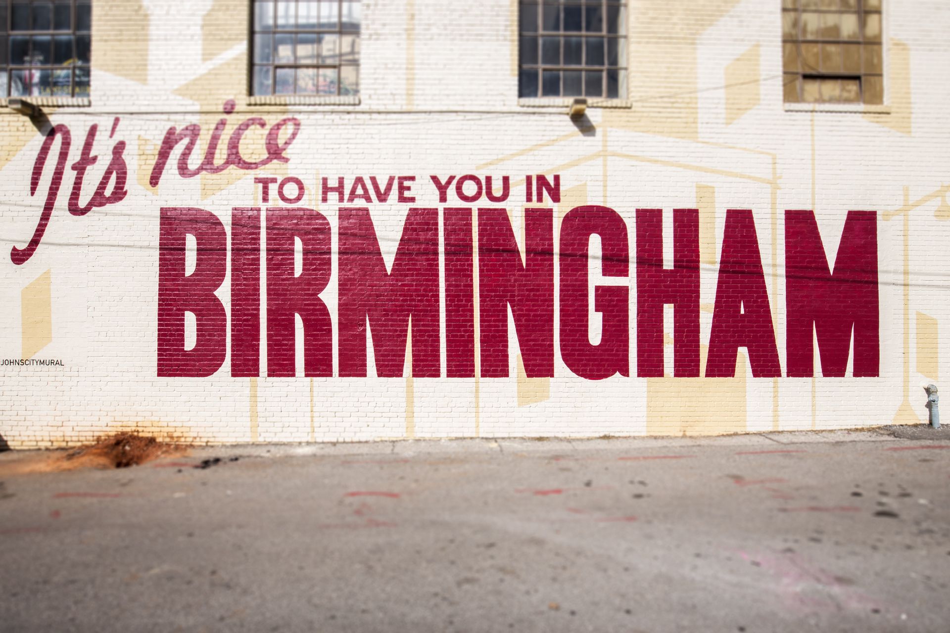 Wall mural reading “It’s nice to have you in Birmingham” in red and pink lettering on a brick wall