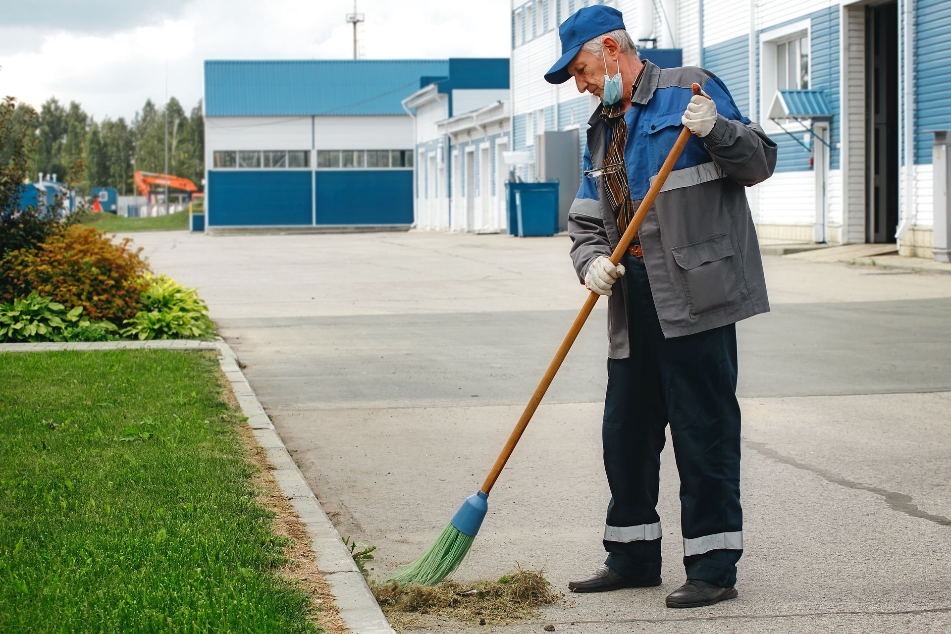 Man in blue cap sweeping a sidewalk outside a blue-and-white building