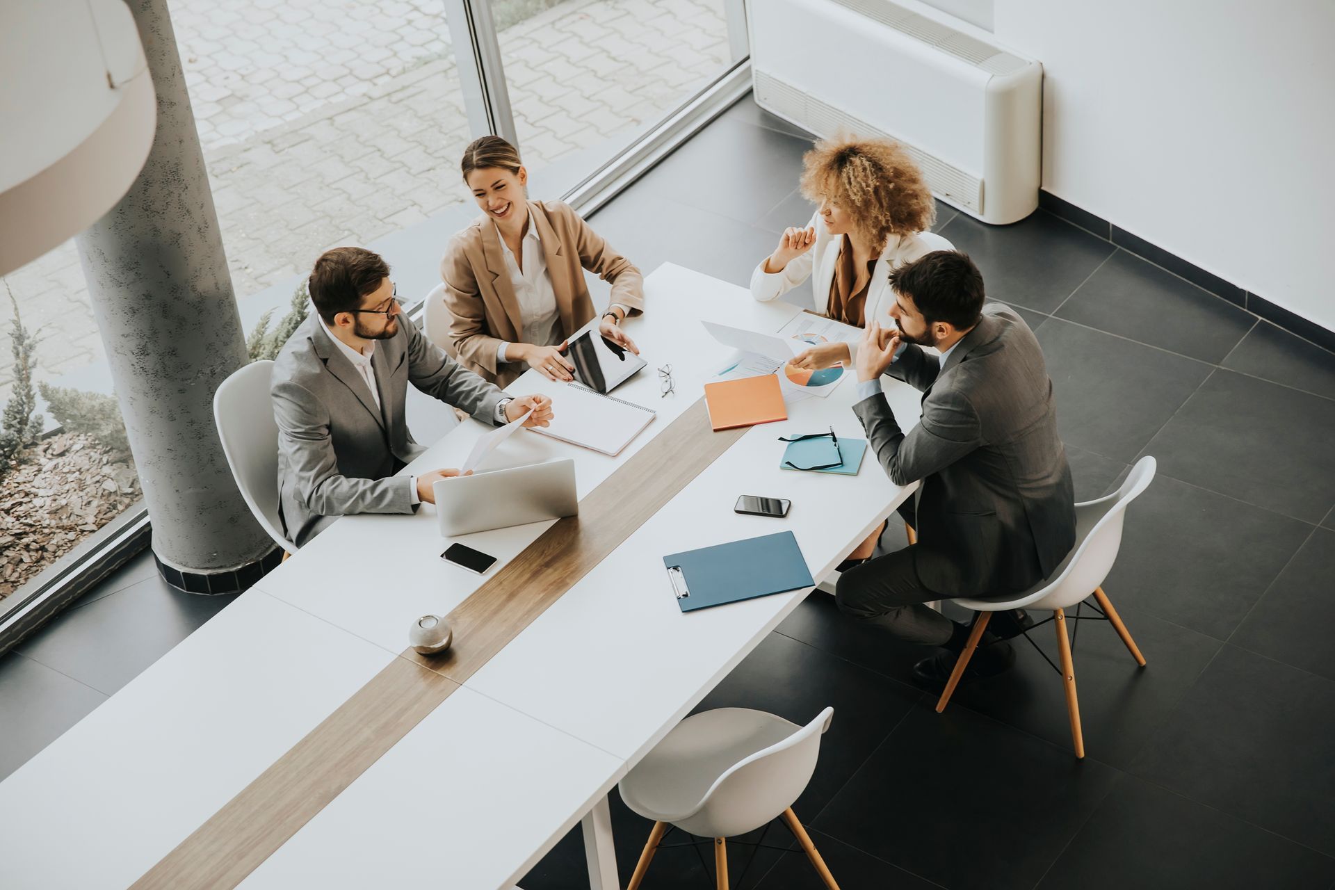 Four coworkers gathered around a white table in a bright office, reviewing documents and discussing work