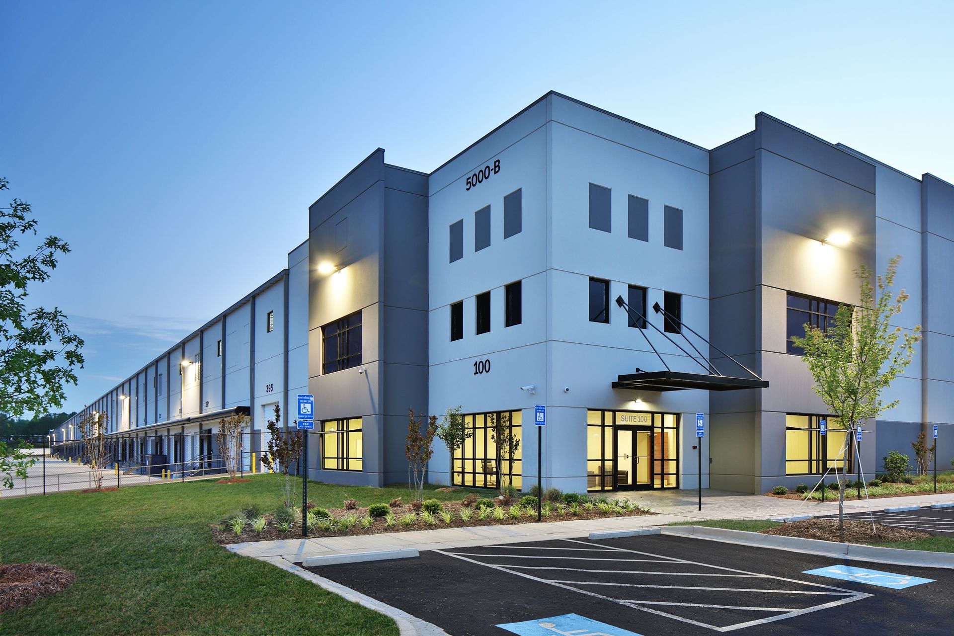 Modern blue-gray apartment complex at dusk with lit entrance and parking lot Modern blue-gray apartment complex at dusk with lit entrance and parking lot