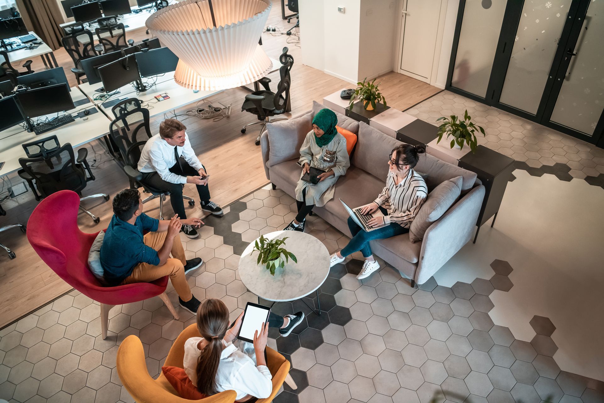 People seated in a modern lounge area in a circle, talking around small round tables.