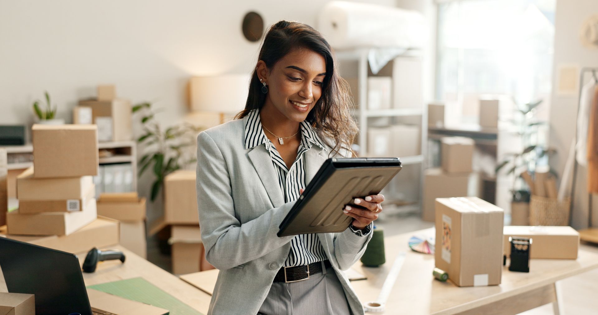 Person in a bright office holding a tablet and reviewing packages on a desk Person in a bright office holding a tablet and reviewing packages on a desk