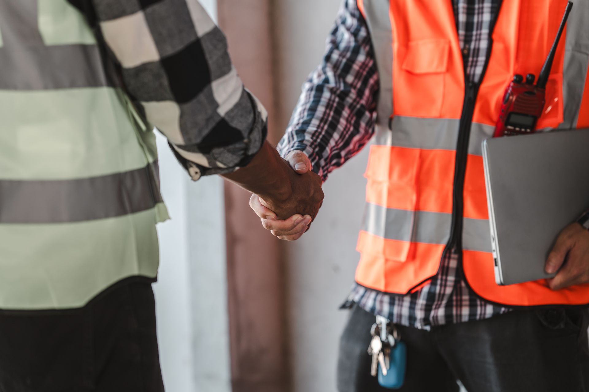 Two workers in safety vests shake hands, one holding a clipboard