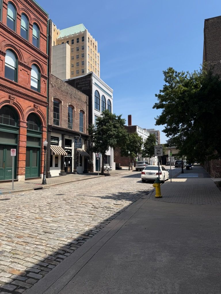 Cobblestone street lined with historic brick buildings under a clear blue sky, with a yellow fire hydrant in front.