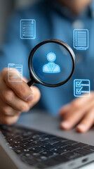Person holding magnifying glass over a user icon, with document icons, near laptop.