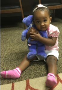 A little girl is sitting on the floor holding a purple teddy bear