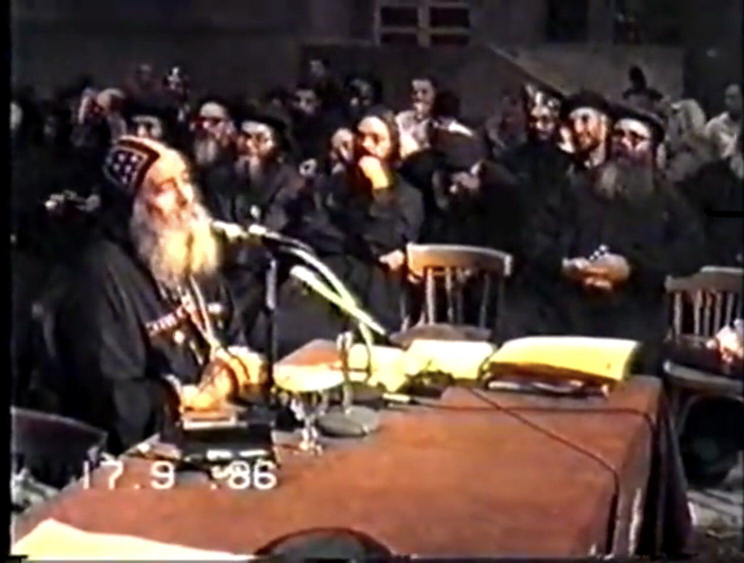 A man is sitting at a table with a microphone in front of a crowd of people ..