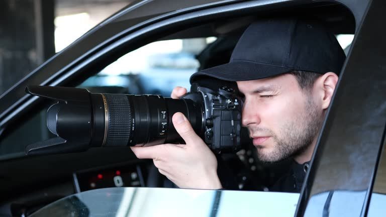 Man in a black cap takes a photo with a large camera from a car window.