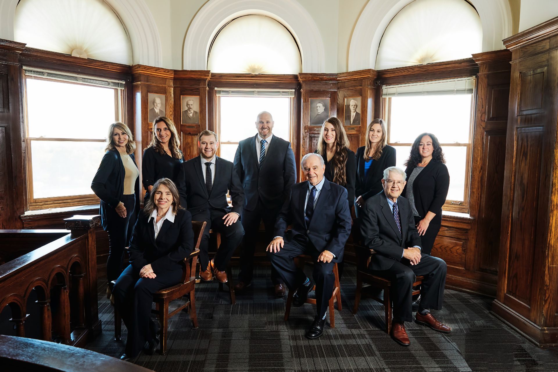 Group of people in suits posing in a wood-paneled room with arched windows.