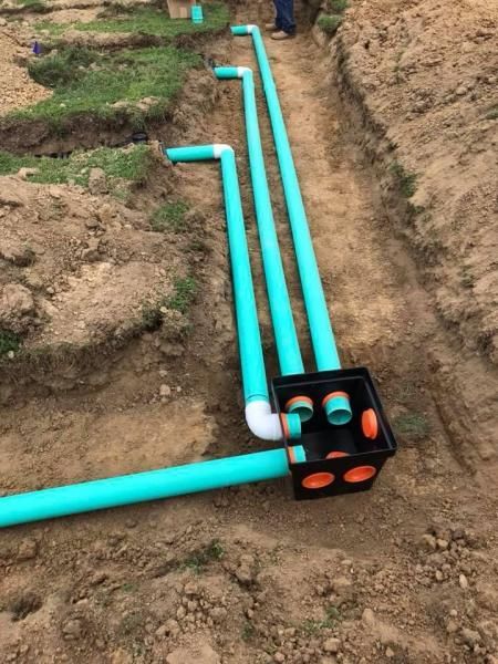 Turquoise PVC pipes laid in a trench beside a black junction box with orange caps on dirt ground