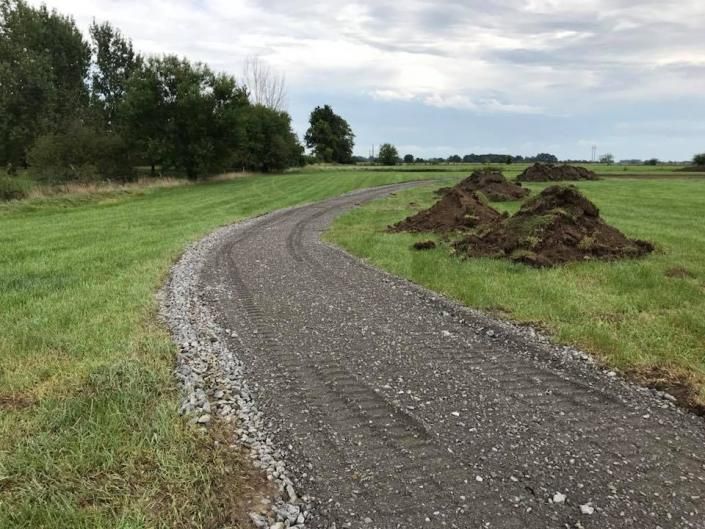 Curving gravel path through a grassy field beside piles of dirt under a cloudy sky