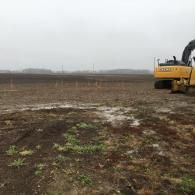 Yellow excavator on muddy farmland under a gray sky