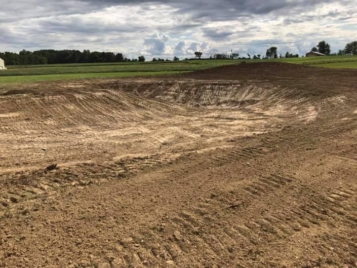 Bare dirt landscape with a large excavated pit under a cloudy sky.
