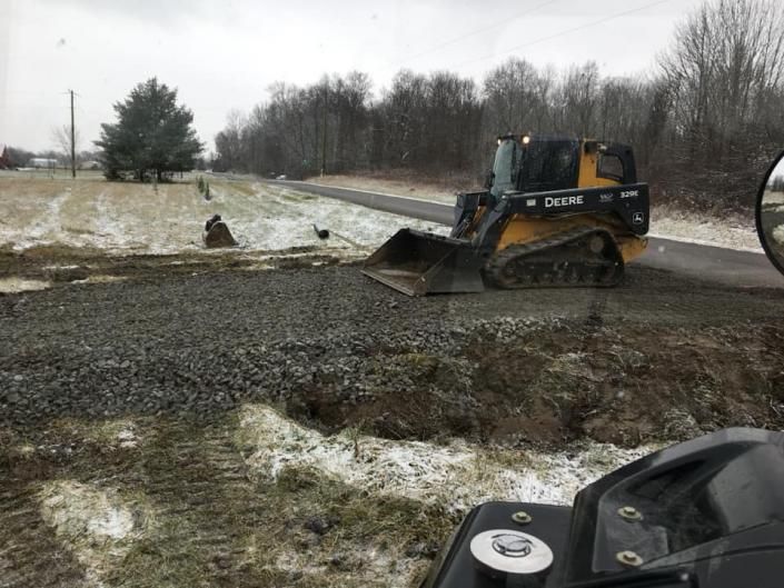 Bulldozer moving mud on a snowy roadside with trees and patchy grass nearby