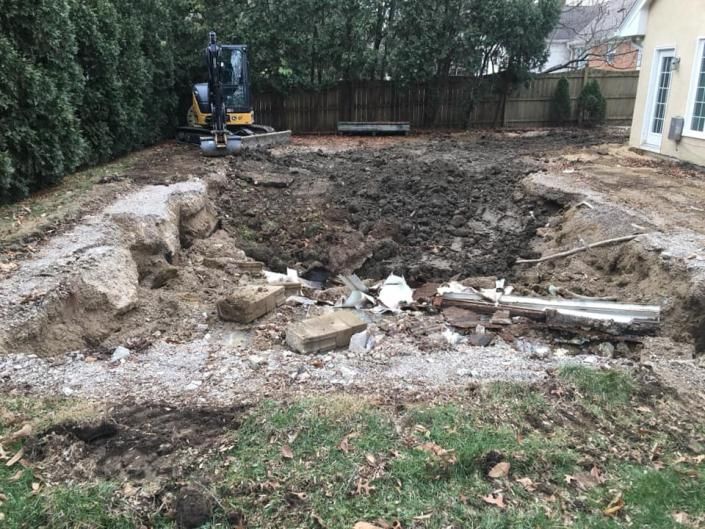 Backyard excavated for construction, with a small digger and piles of dirt and debris.