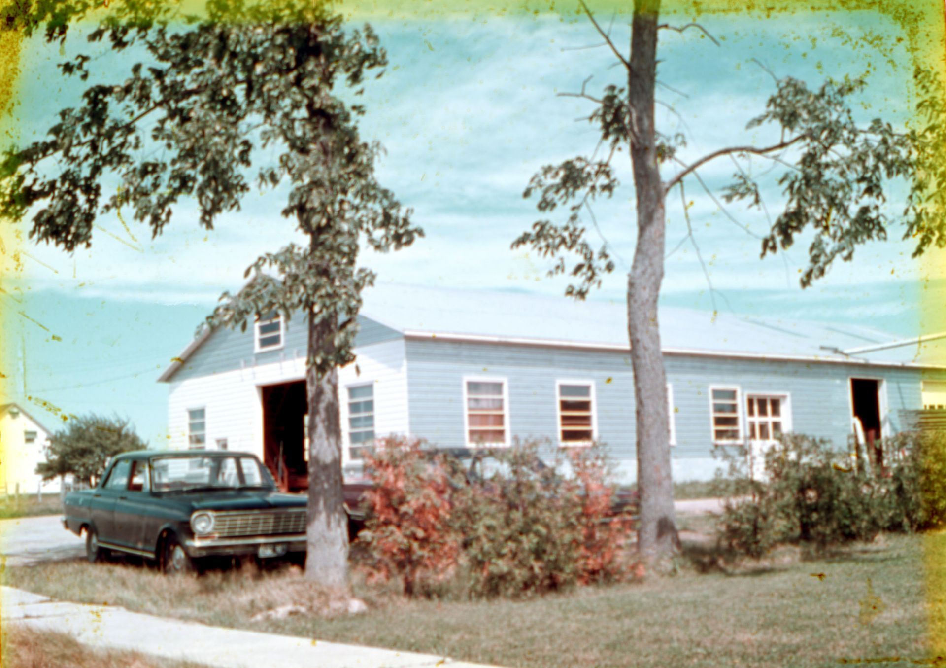Grange bleue aux portes ouvertes, voiture verte et arbres.