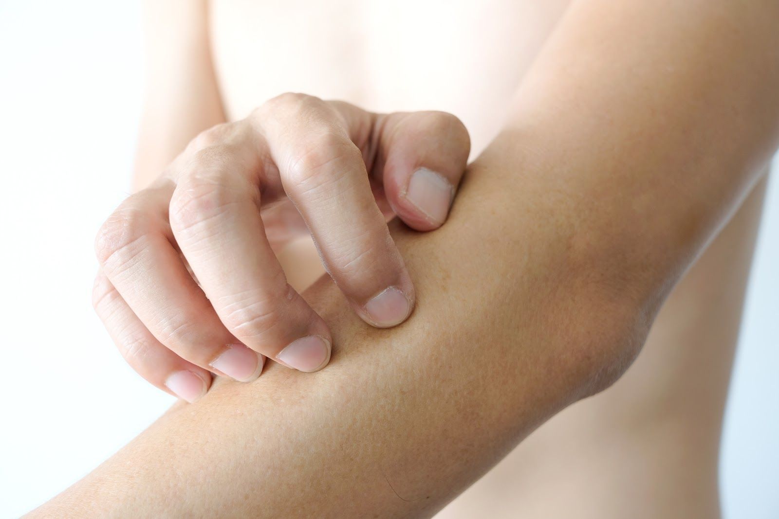 A hand scratching an itchy forearm on a white background