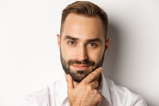 a man with a beard is holding his hand to his chin and smiling .