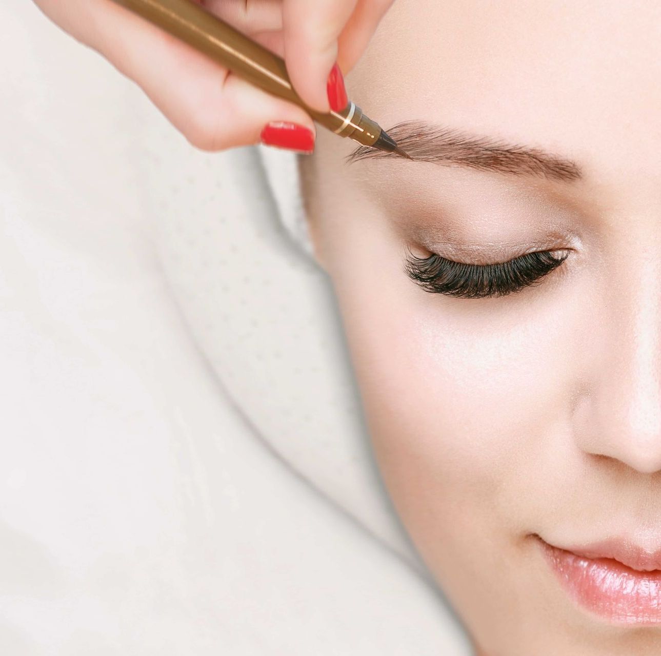 a woman with red nails is getting her eyebrows done