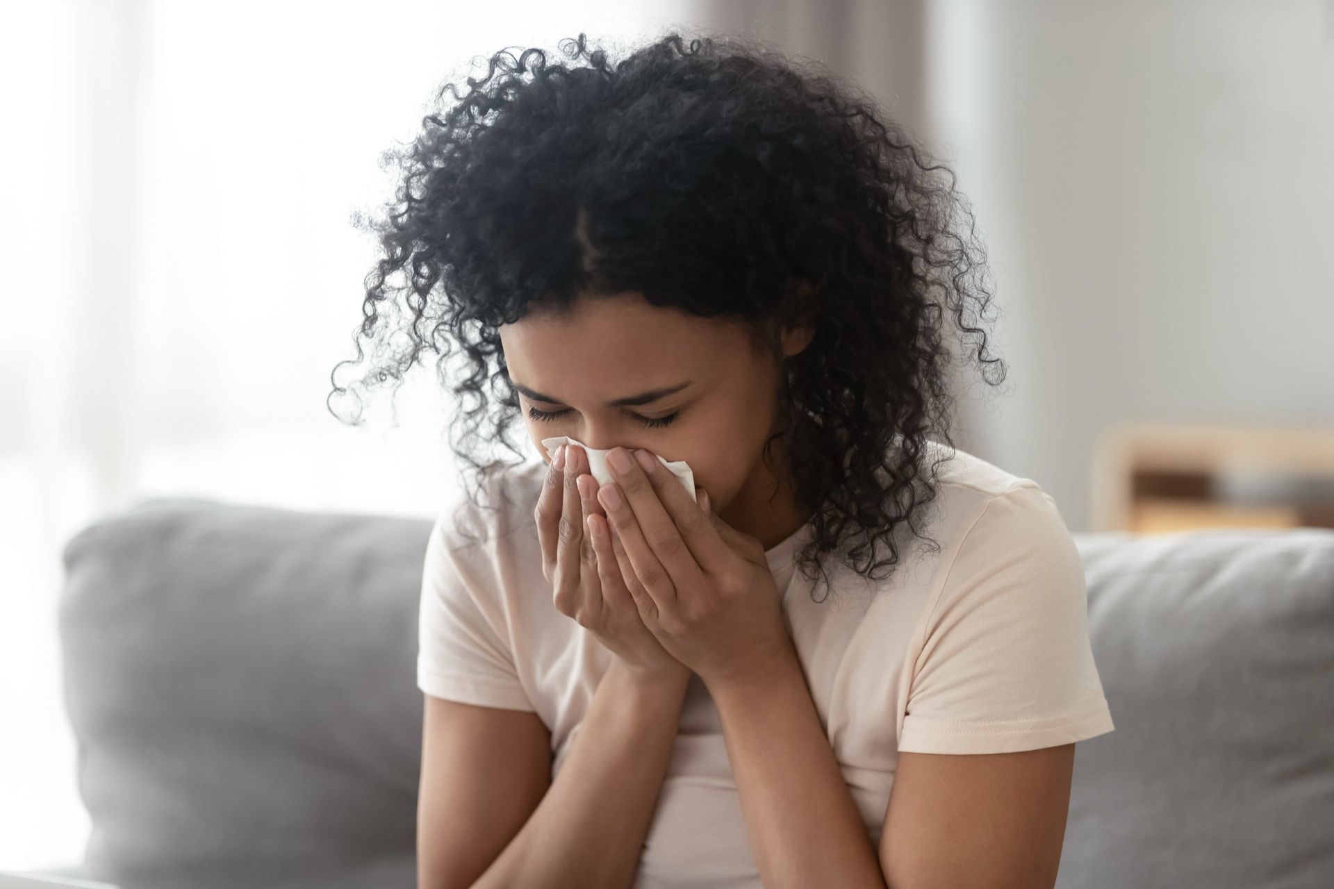 a woman is blowing her nose into a napkin while sitting on a couch .