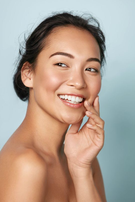 a woman is smiling and touching her face with her hand .