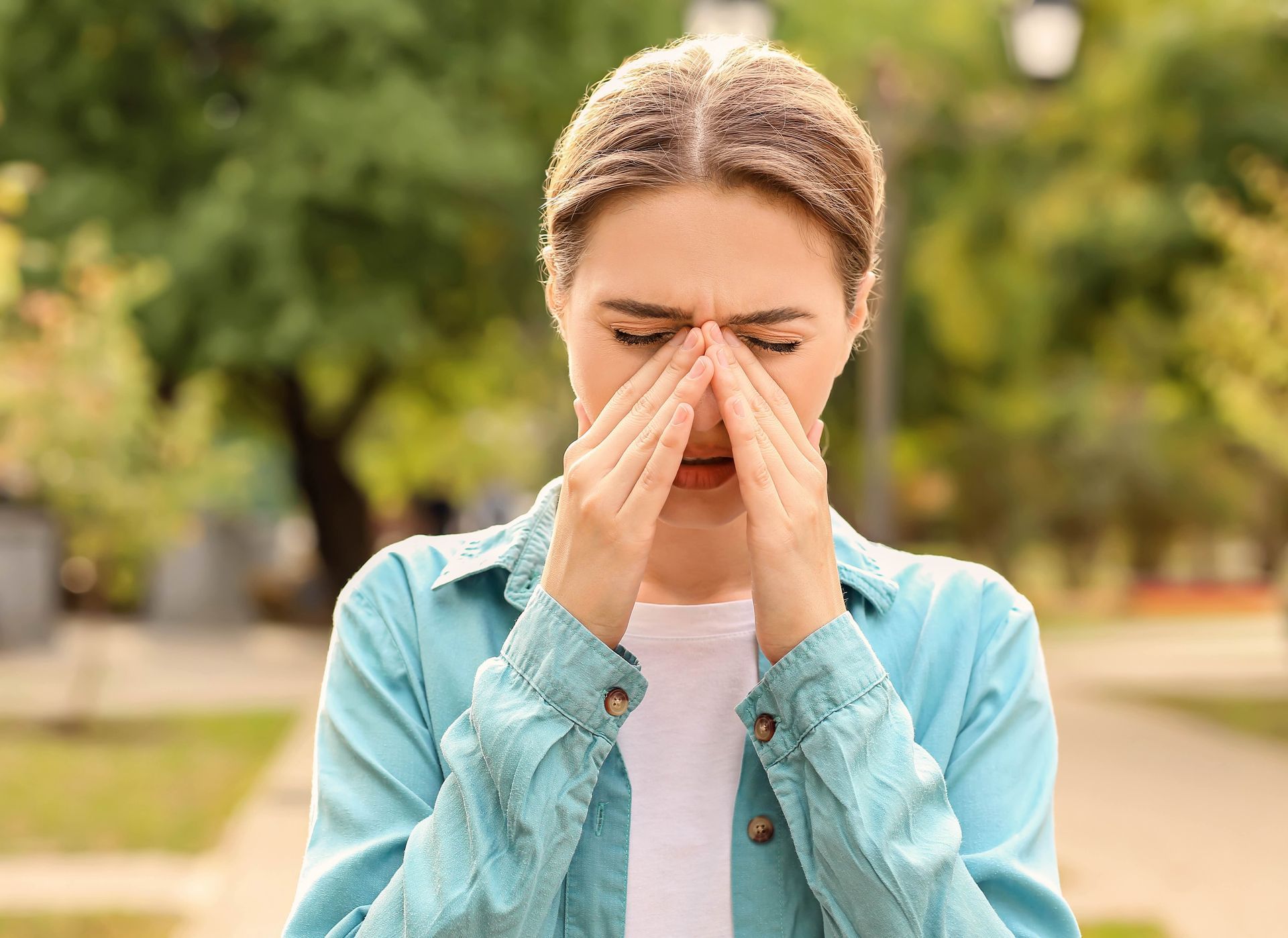 a woman is covering her nose with her hands in a park .
