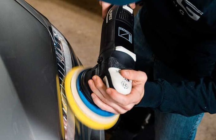 A person is polishing a car with a machine.