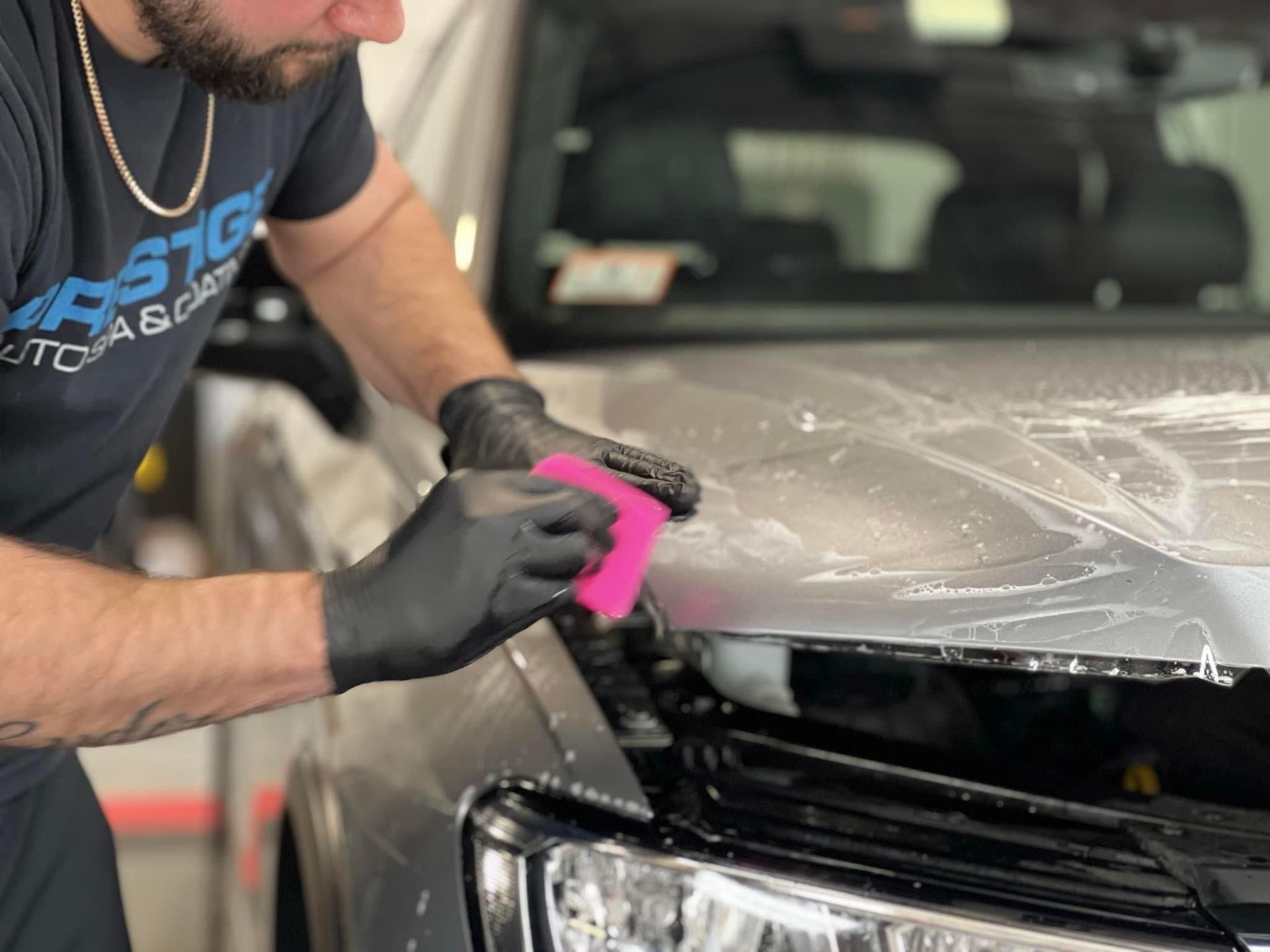 A man is cleaning the hood of a car with a pink sponge.