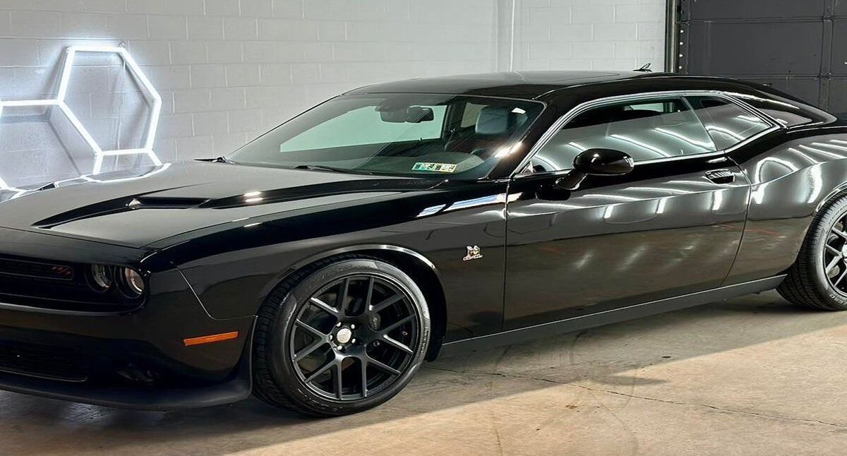 Black Dodge Challenger parked in a garage with a hexagonal neon light on the wall.