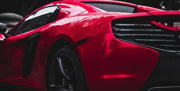 A close up of a red sports car parked in the rain.