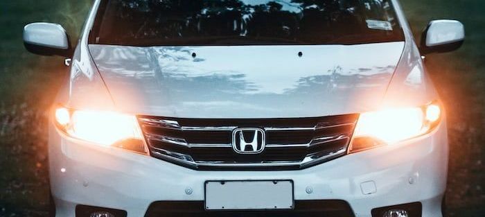 A close up of a white honda car with its headlights on.