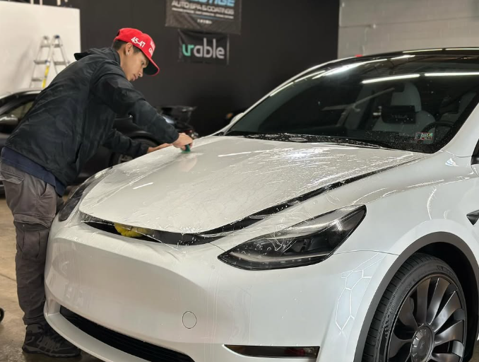 A man is applying PPF on a white Tesla Model Y in a garage.