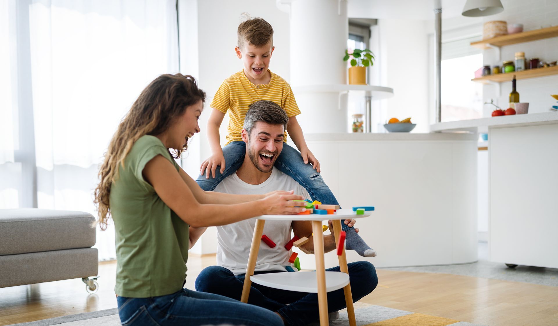 A family is sitting on the floor in a living room playing with toys.